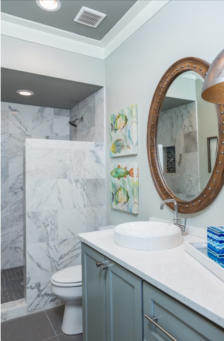 Coastal new construction bathroom, tile shower, blue vanity, porthole mirror, colorful fish details