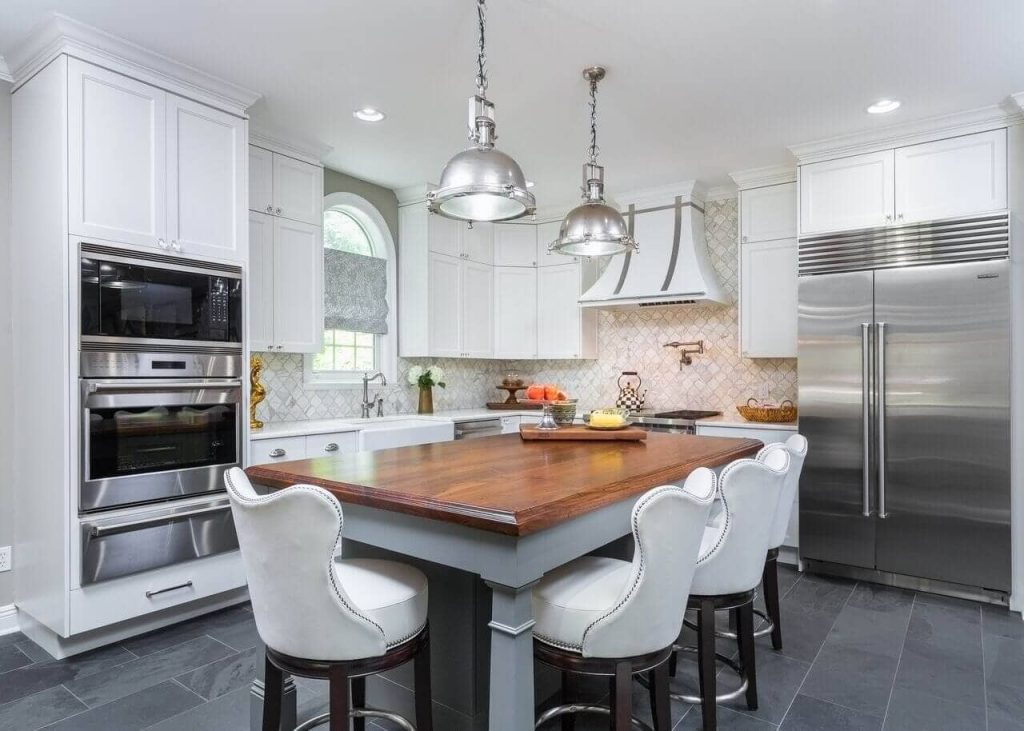 Slate tile, white kitchen cabinets, pendants, grey island, upholstered counter stools, mosaic tile backsplash, roman shade, hood vent, wood top, recessed lighting, stainless appliances