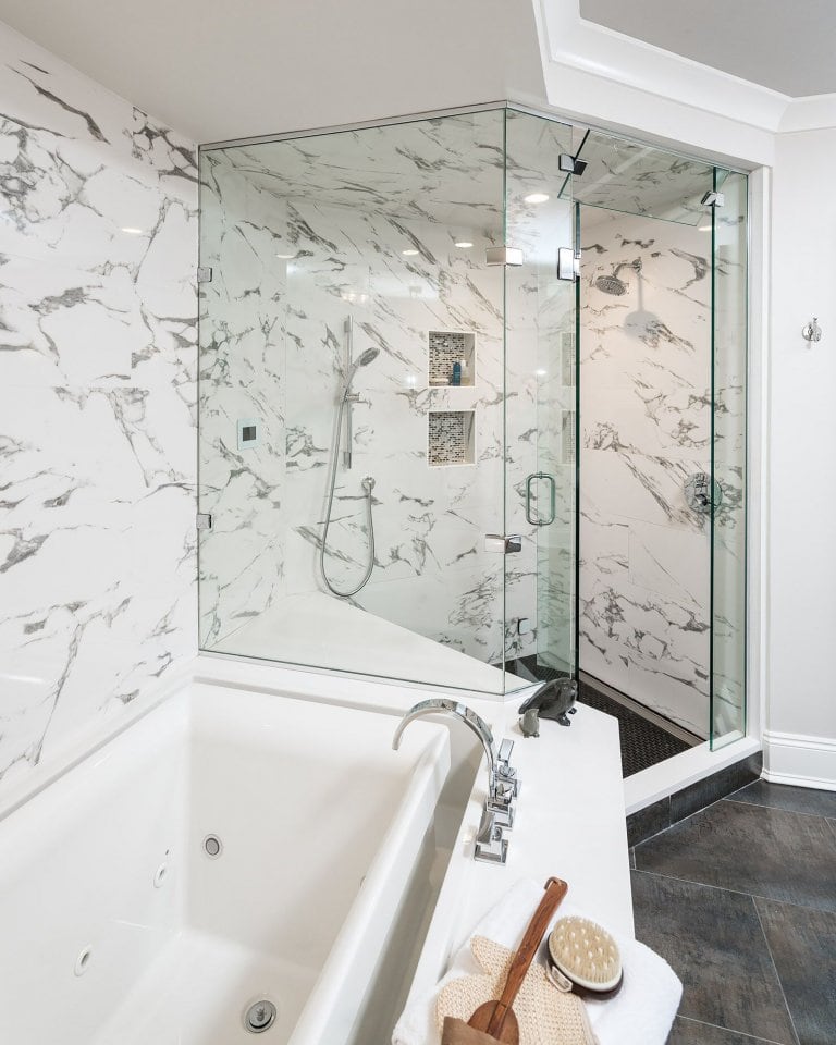 Walk in marble shower with bench and mosaic tile niches connected to an infinity tub.
