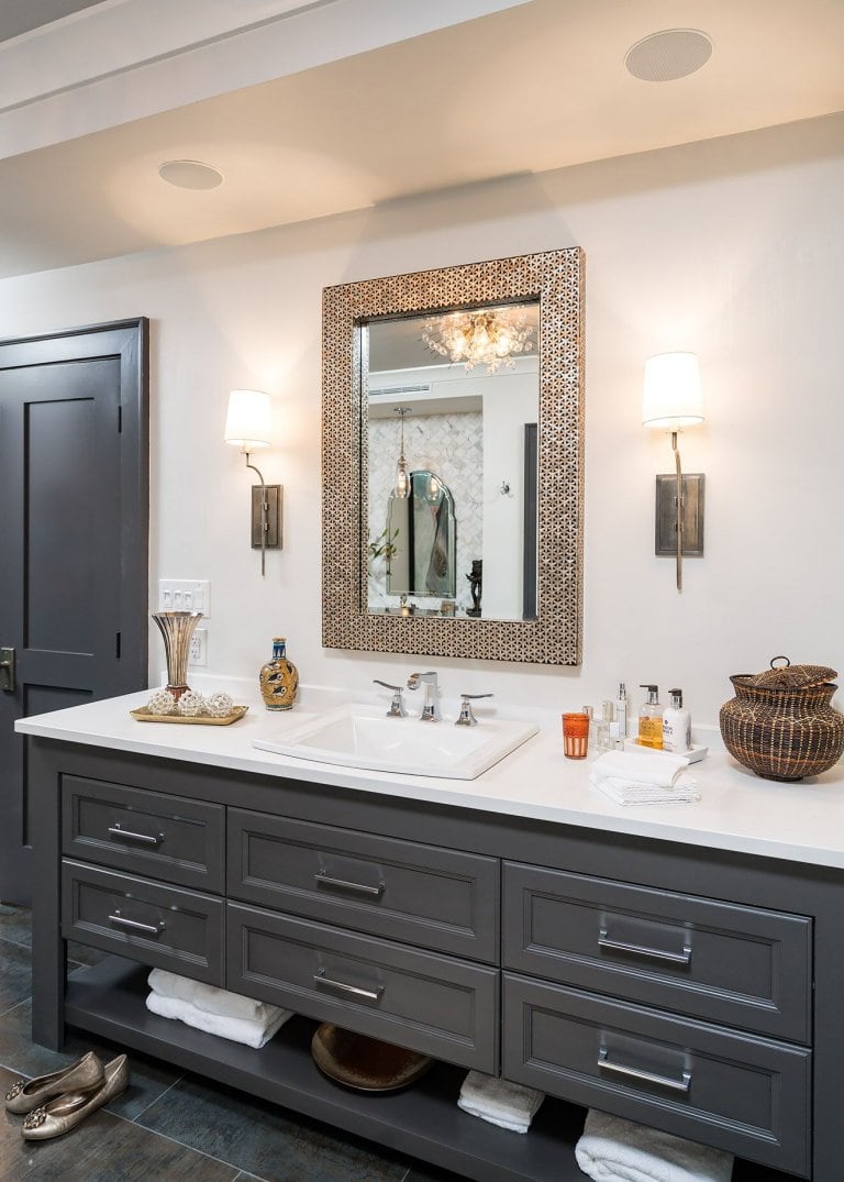 Custom grey Vanity with open bottom shelf, marble countertops with brass mirror and metal sconces.