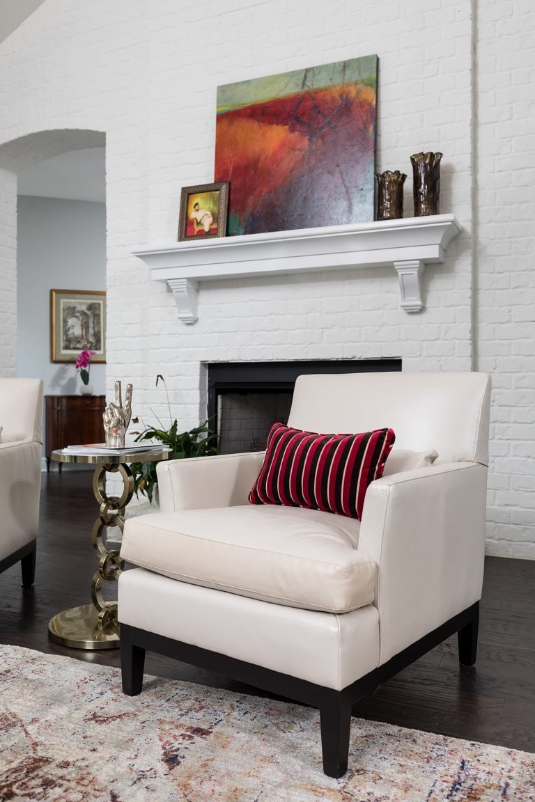 Cream colored accent chairs in front of a painted white brick wall with fireplace. Original art and vintage style rug