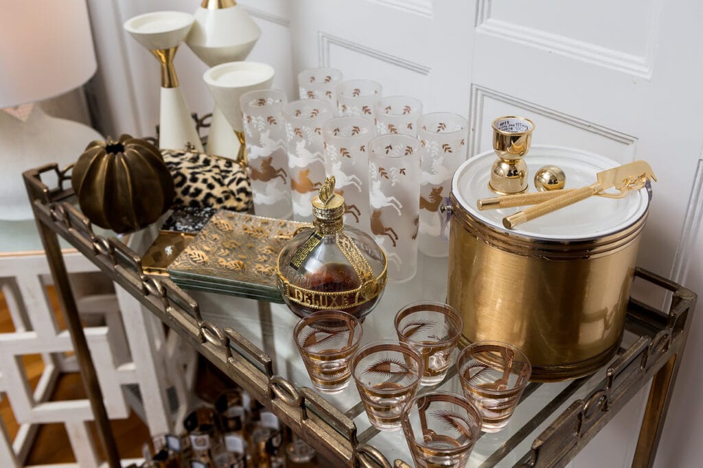 Vintage glassware and ice bucket mixed with modern candle holders styled on a gold and glass bar cart. Vintage tray and fall pumpkin decorate the cart too.