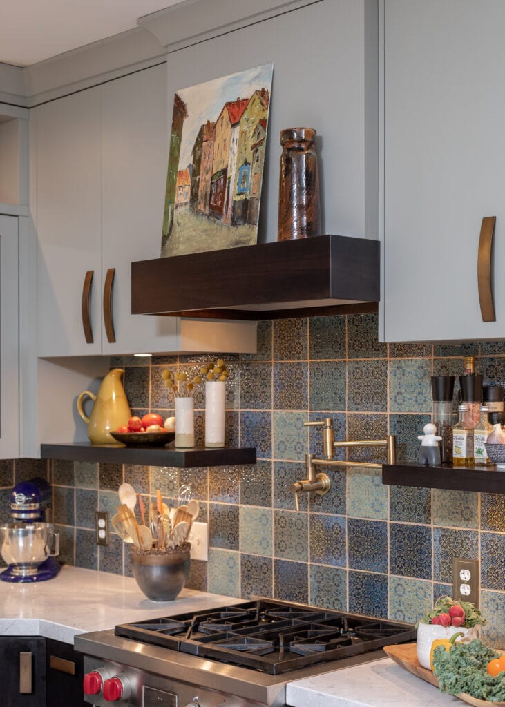 Traditional and eclectic kitchen with colorful and textured tile backsplash. Original art and vintage pottery. Quartz countertops with blue gray cabinets and copper and bronze fixtures and hardware.
