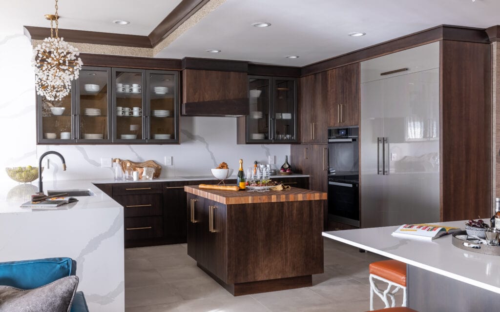Landscape view of modern kitchen with quartz countertops, butcher block countertops, full height quartz backsplash, waterfall end panel on island, stained cabinets, funky and modern pendant lighting. 